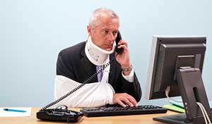 man with neckbrace and arm in sling on phone and computer